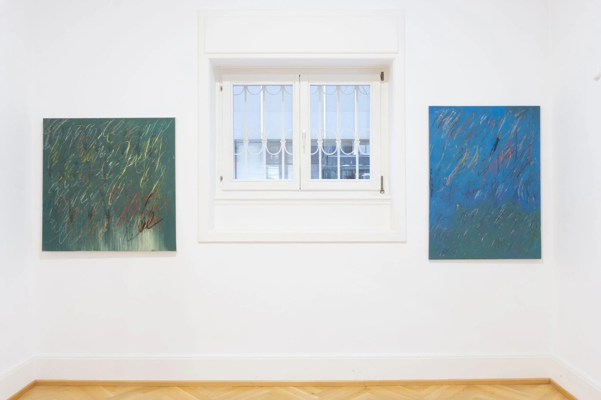 Two abstract paintings on a white gallery wall, with a window in the center showing an outdoor scene.