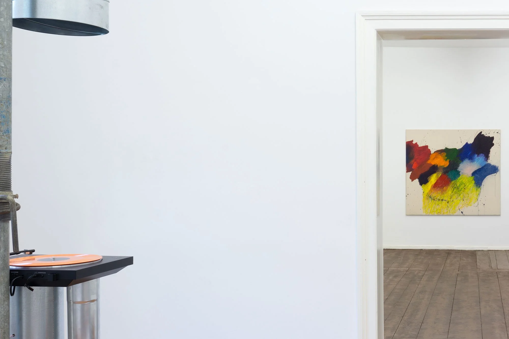 Part of an art gallery with a colorful abstract painting on the wall and a corner of a table with a record player.