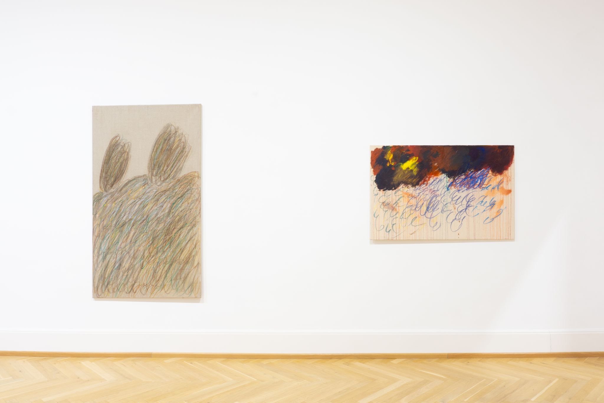 Two abstract paintings on a white gallery wall, with a light wooden floor.