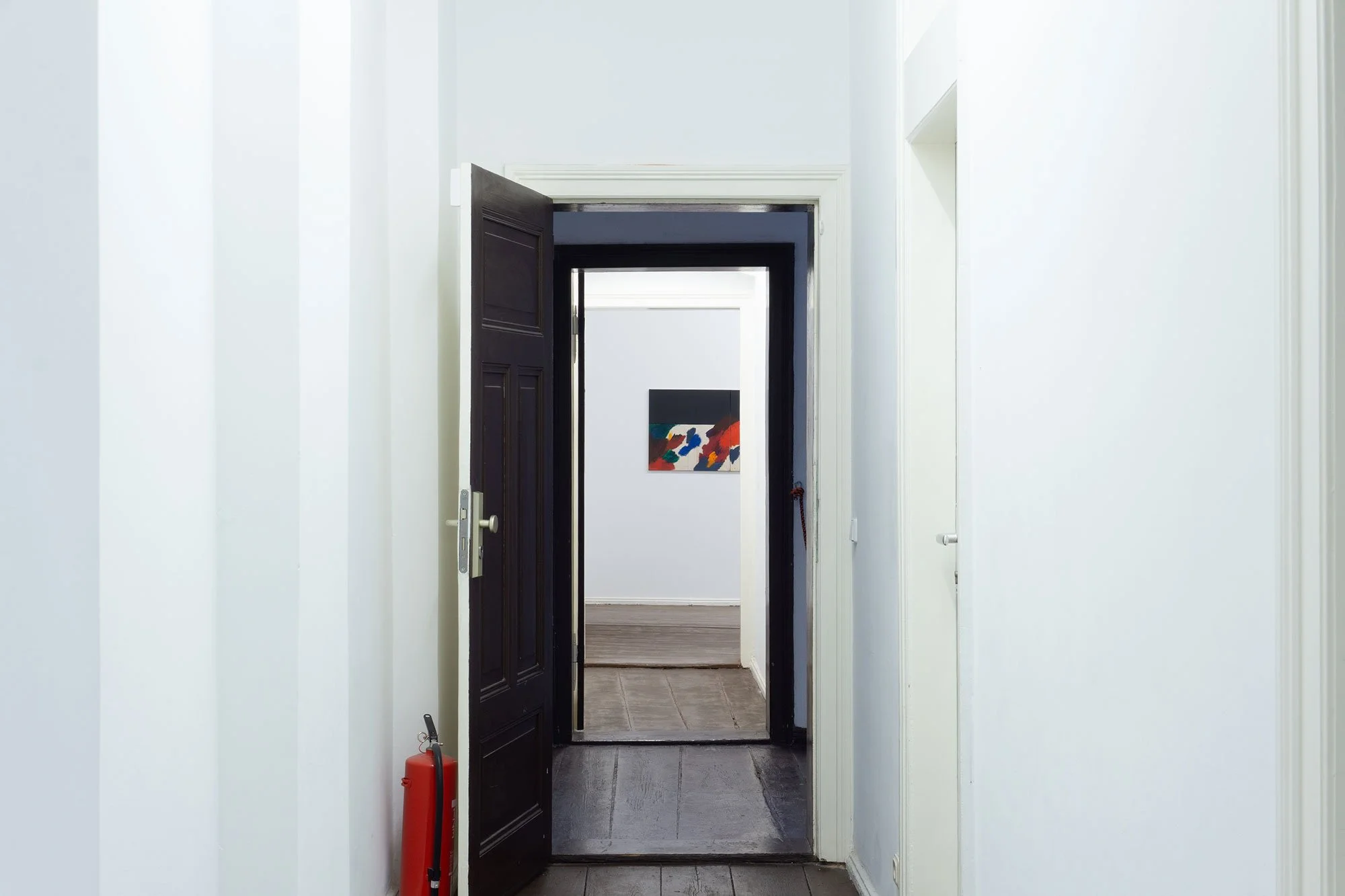 Interior of a house with a black front door slightly open, white walls, and a fire extinguisher on the left side.