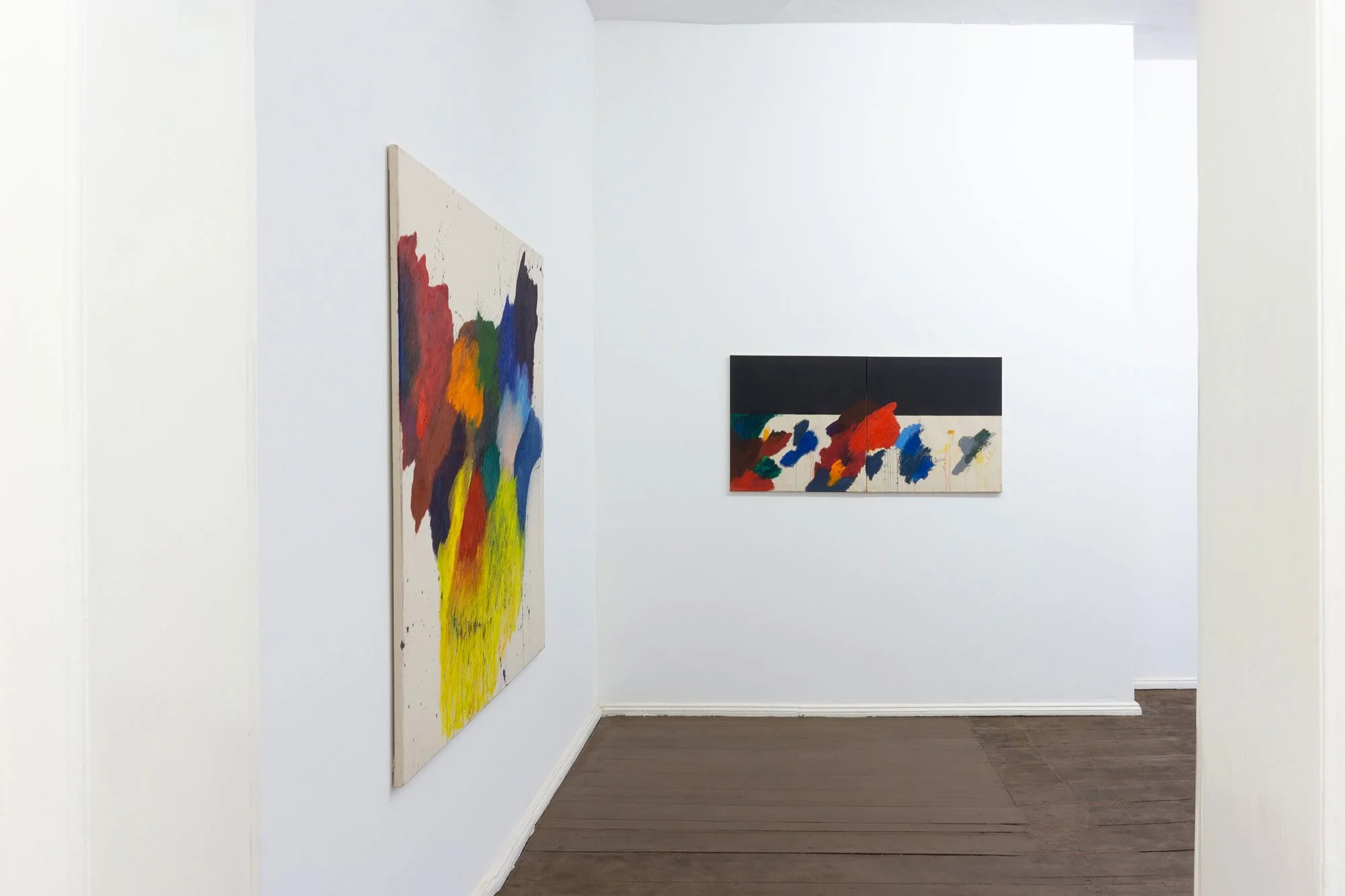 Art gallery with two colorful abstract paintings on white walls and a hardwood floor.