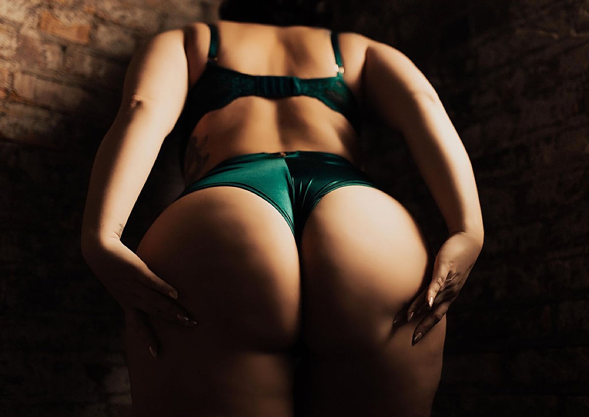  woman in green lingerie poses with hands on hips during repeat client love boudoir session. 