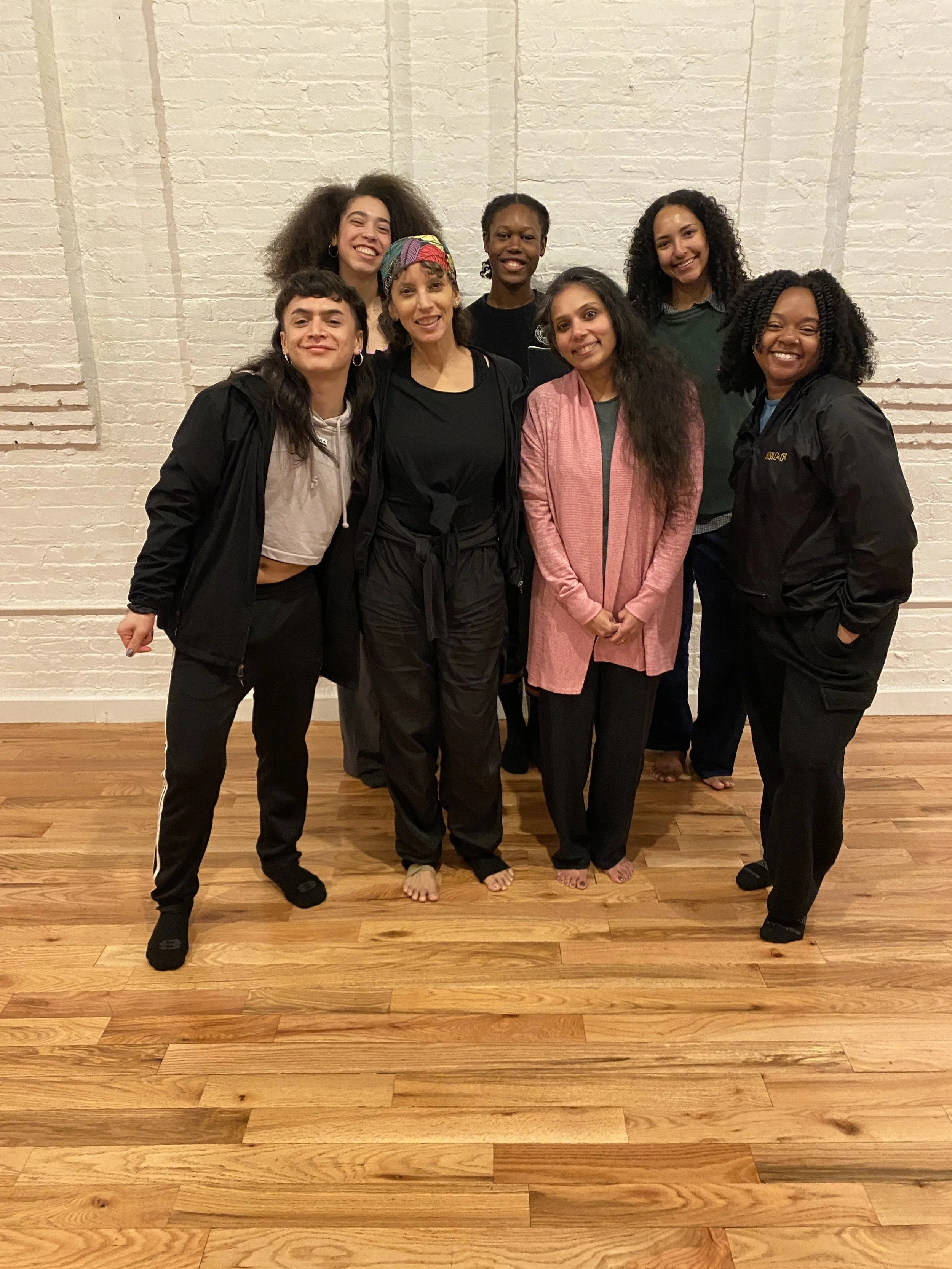 A color photograph of seven of the Collective Thread Residency Participants in a studio.