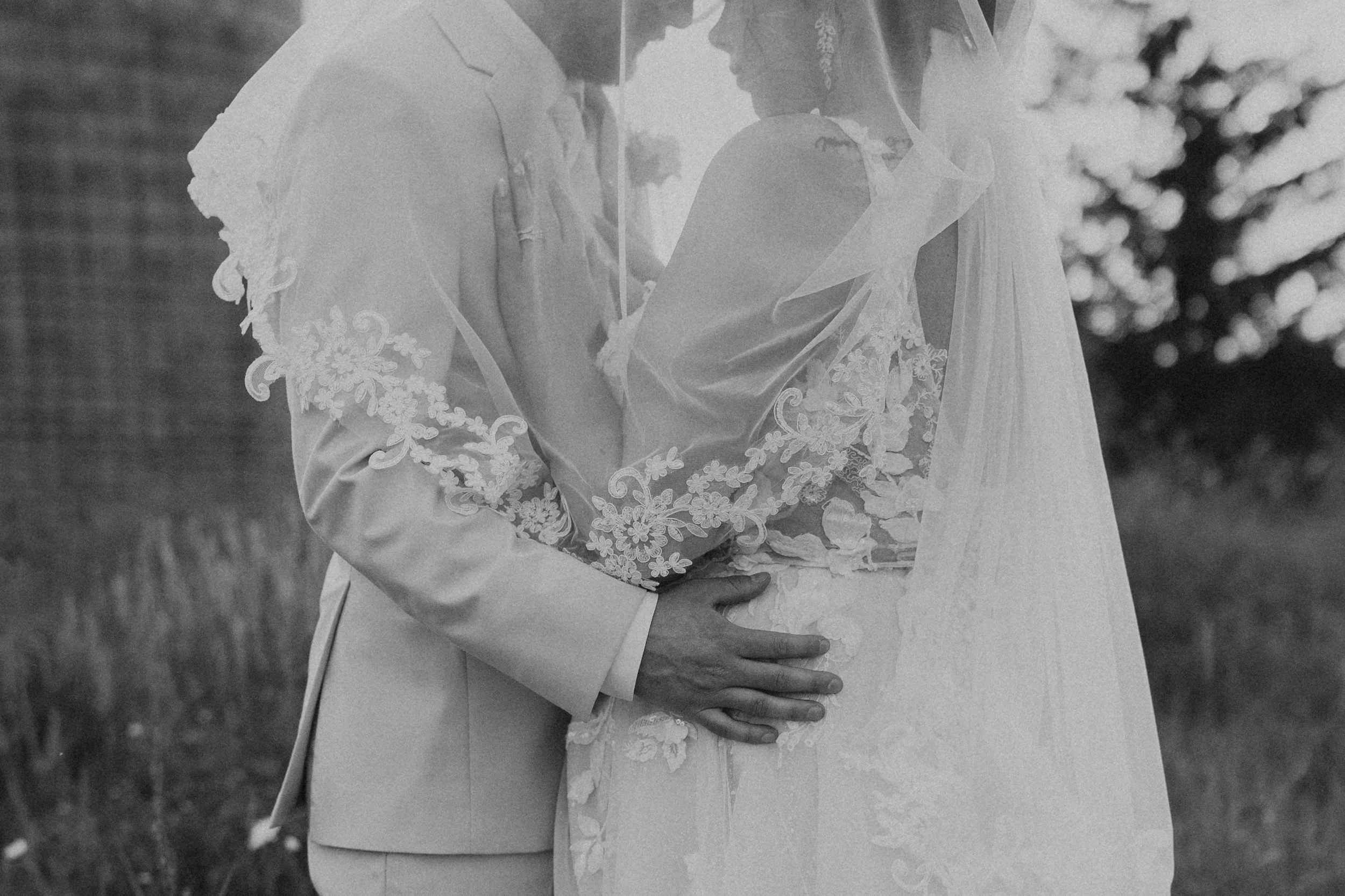 couple in bridal attire embracing under wedding veil