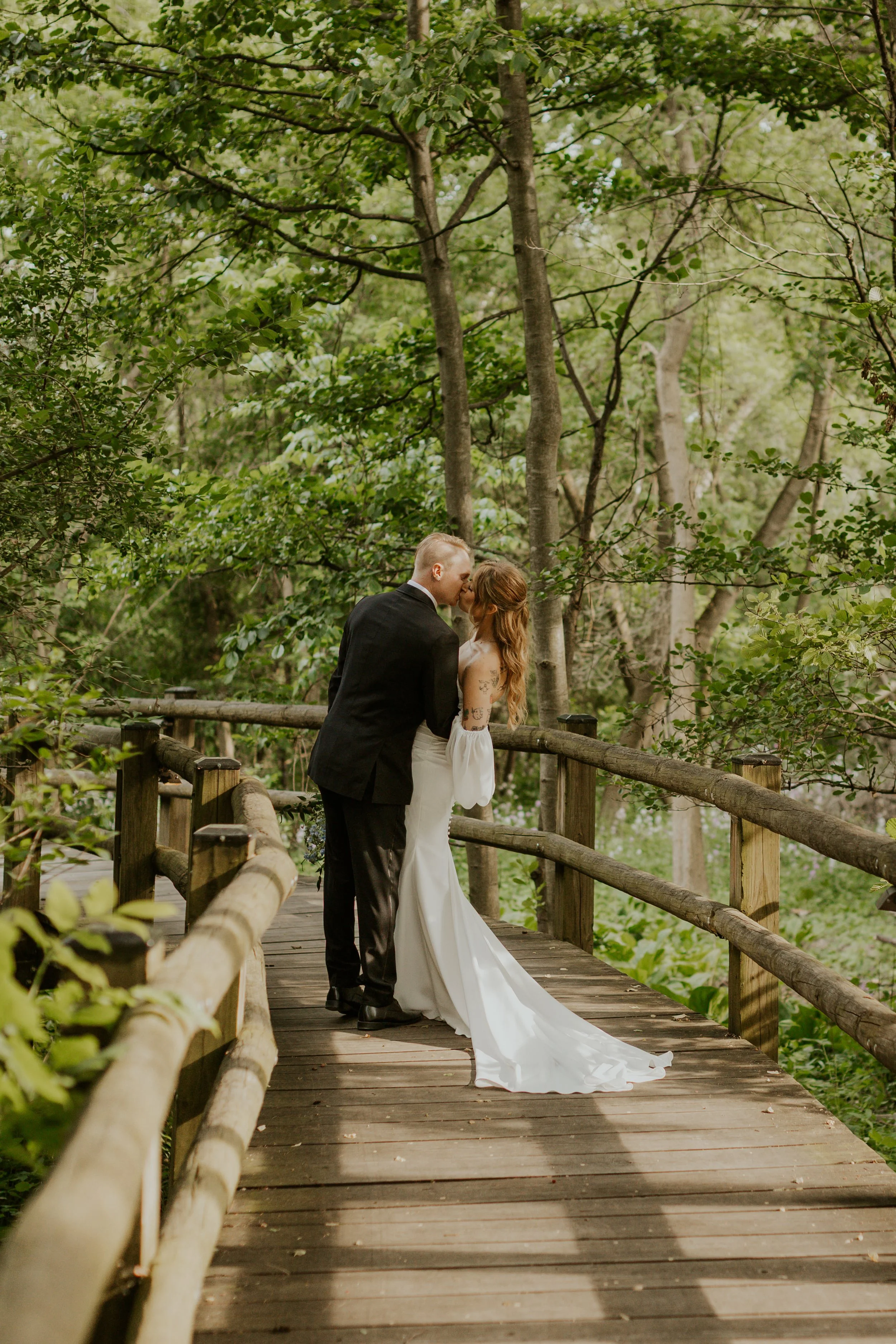 bridal couple dipper for a kiss at sunset on wooded path with lush green background
