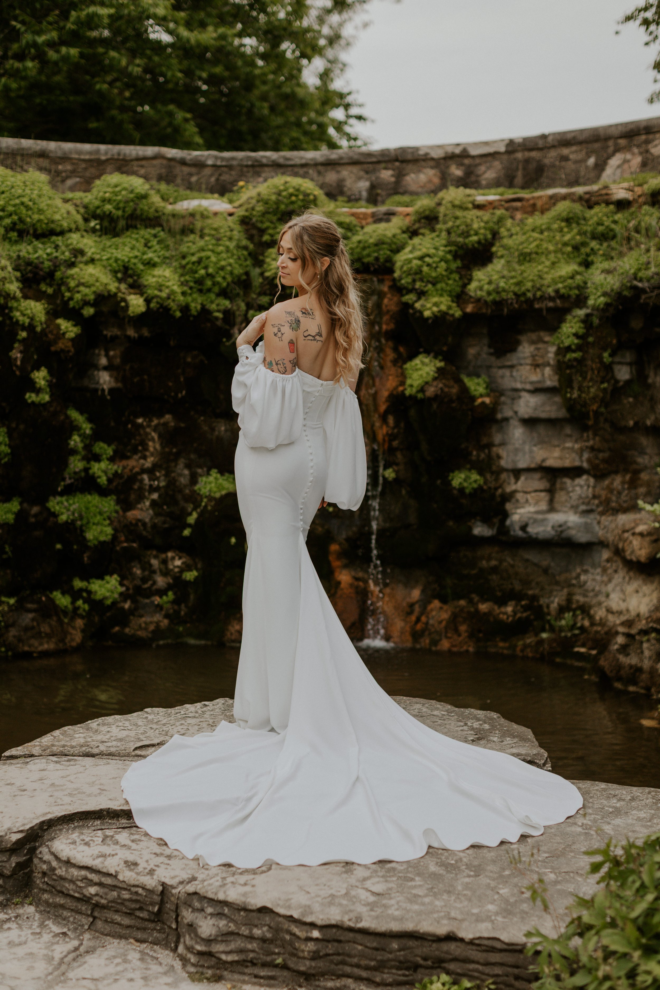 bride posing in wedding attire in front of mossy rock wall feature in boerner botanical gardens