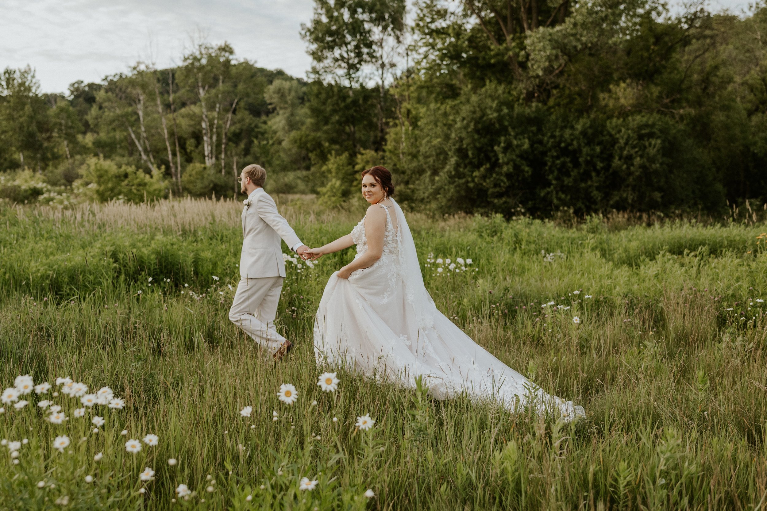 bridal couple walking through grassy meadow with white wildflowers
