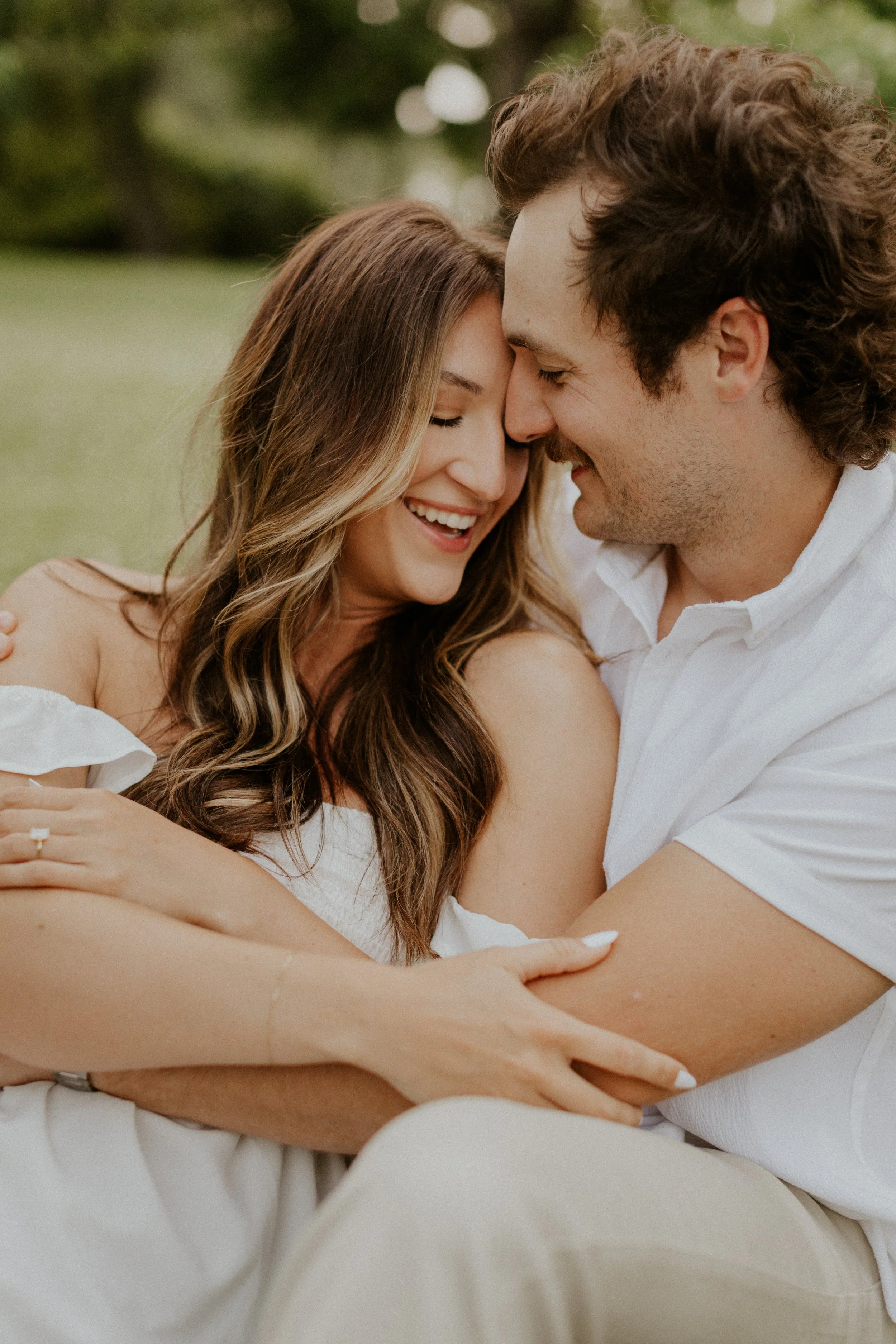 couple snuggling and embracing sitting in the grass at a park in Fort Collins