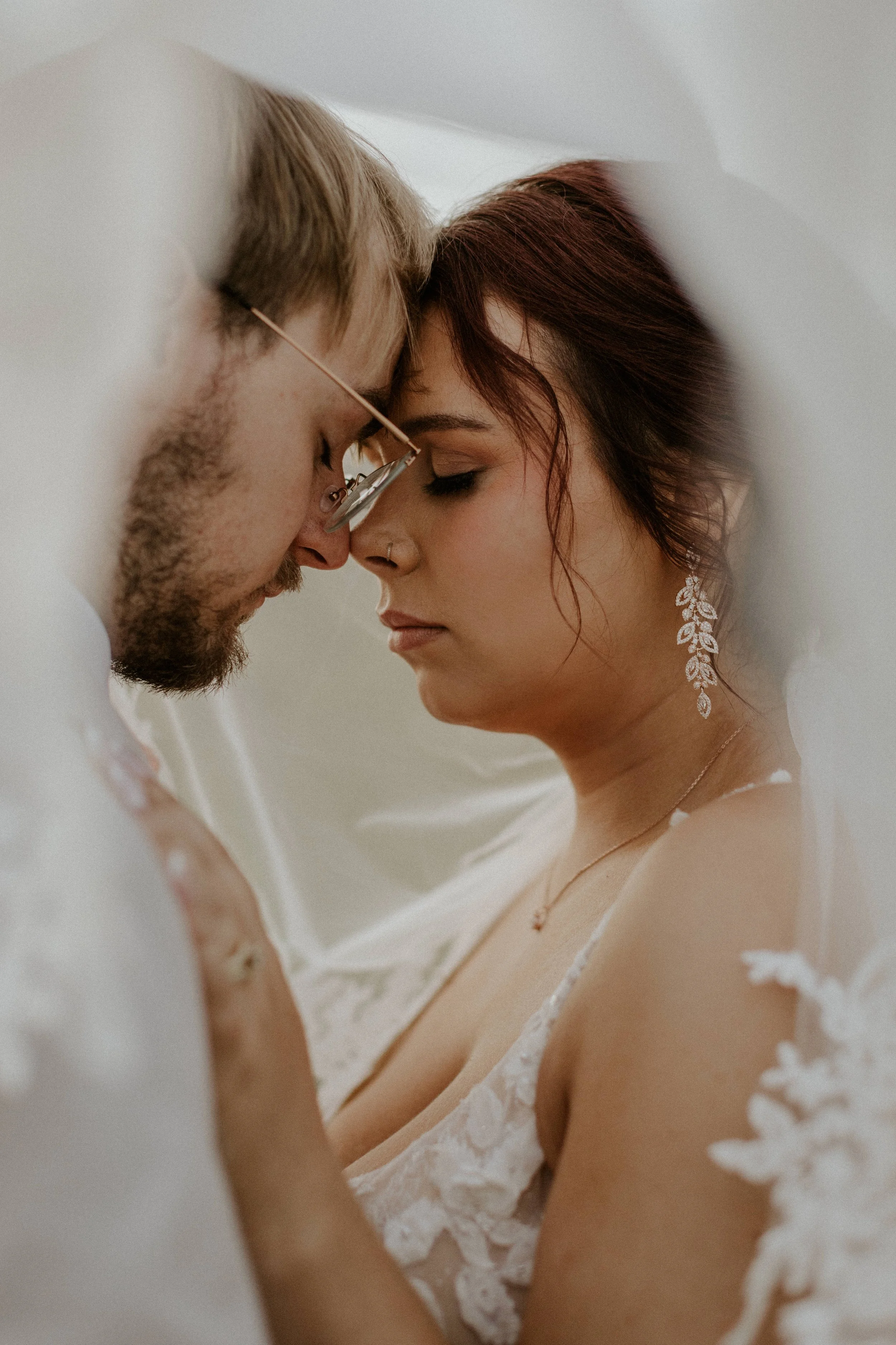 close up of bridal couple leaning together under wedding veil