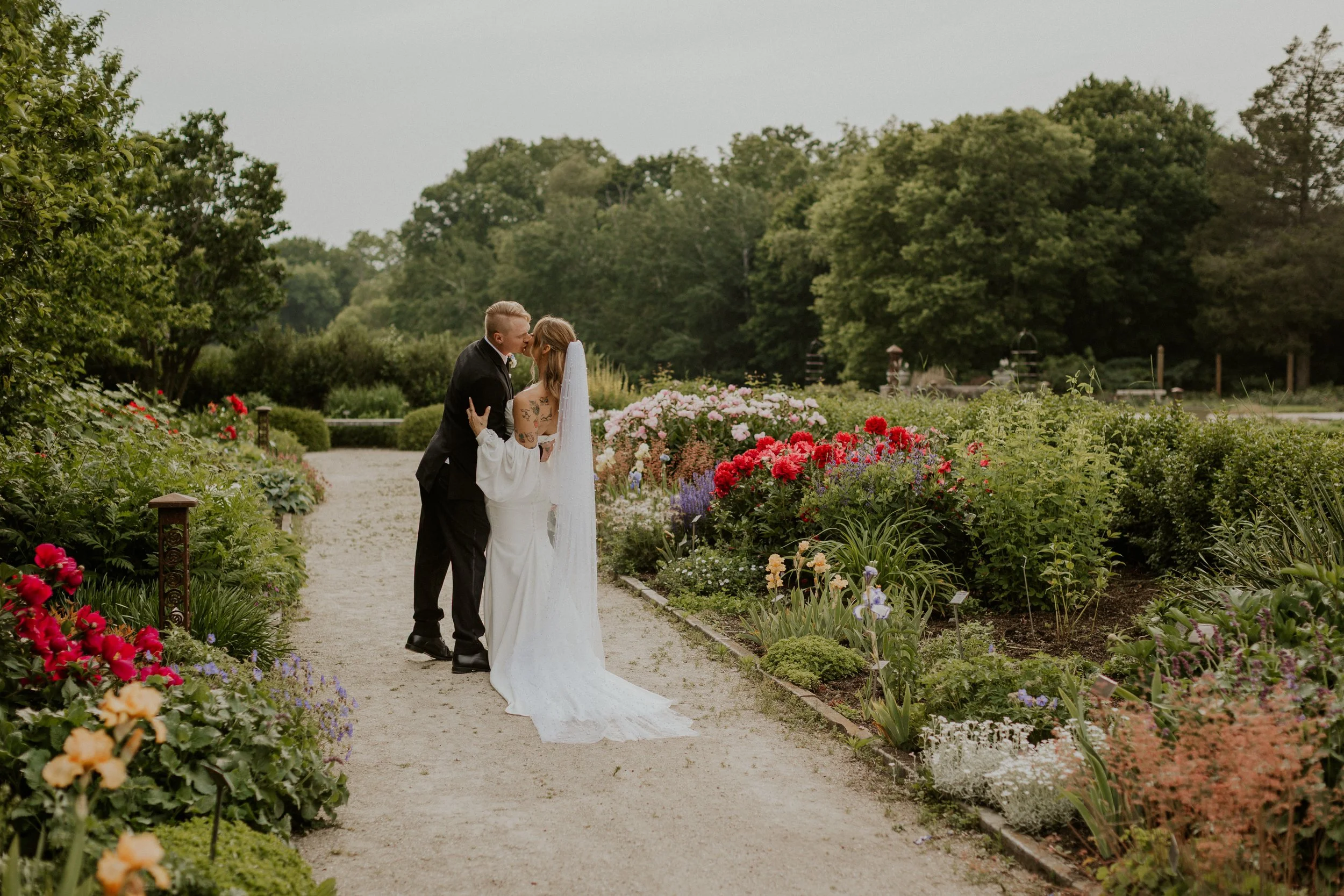 couple in bridal attire dipping for kiss in brightly colored floral garden