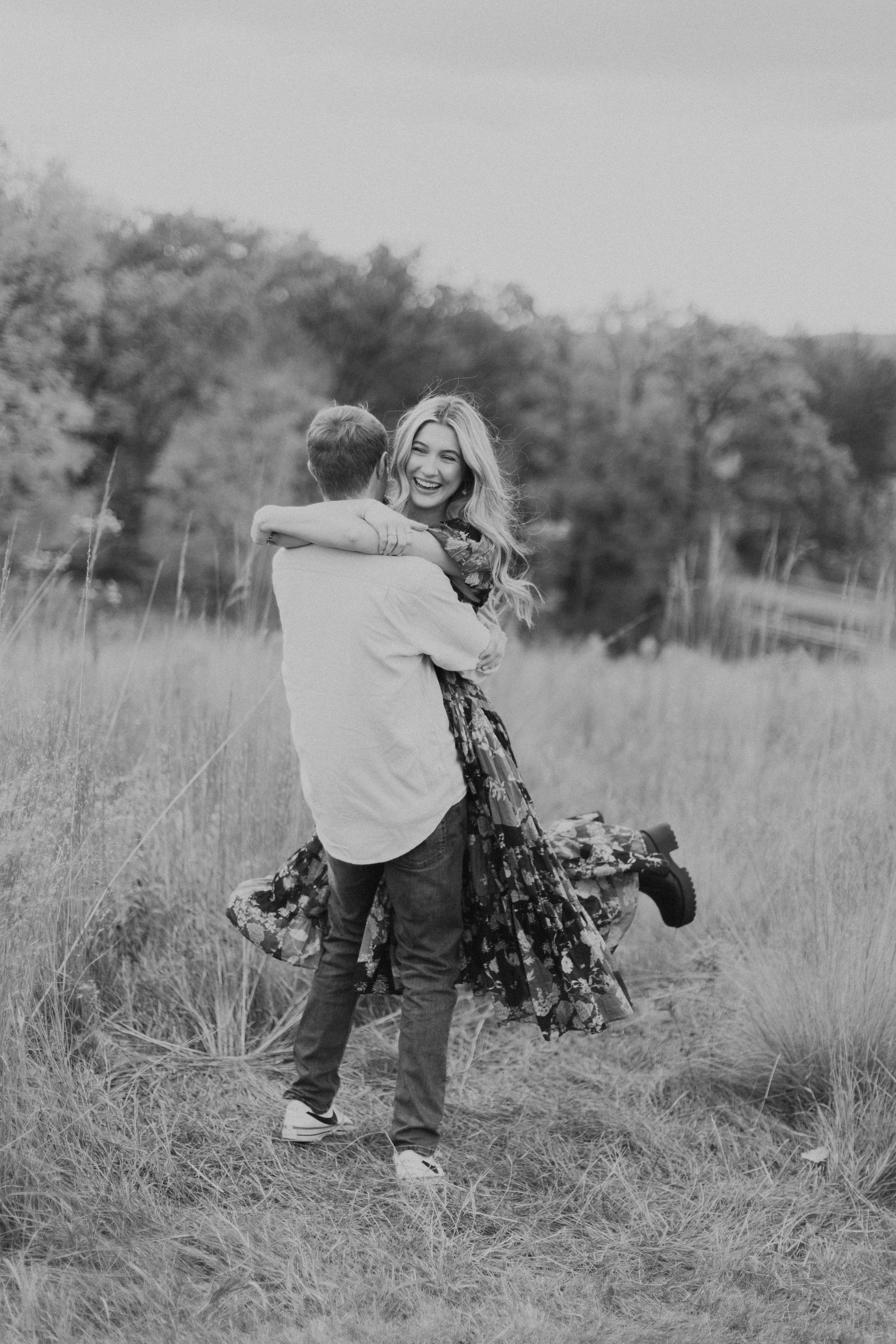 man picking up and spinning girlfriend in long, flowy dress at a park