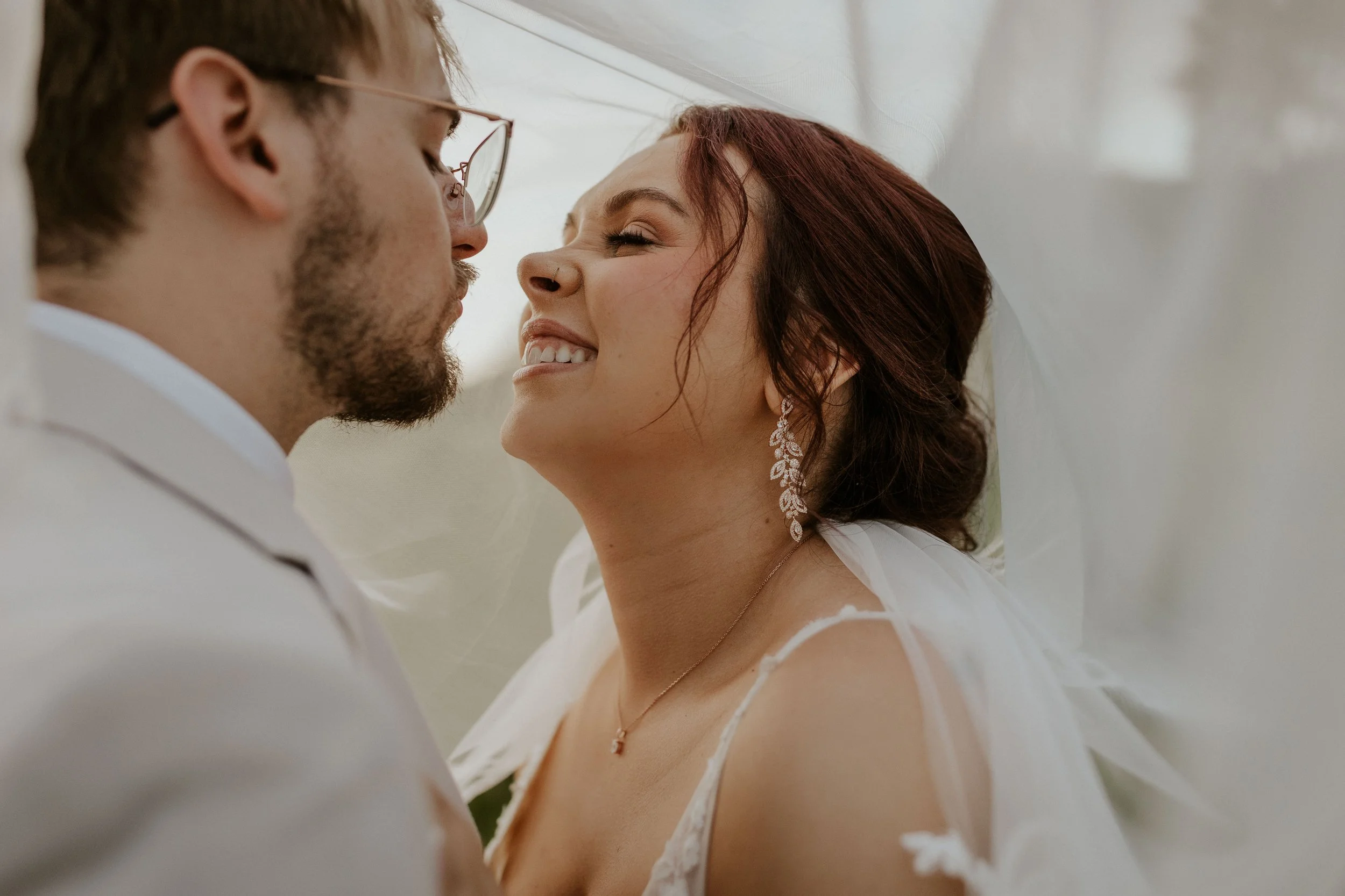 bridal couple smiling close under bridal veil