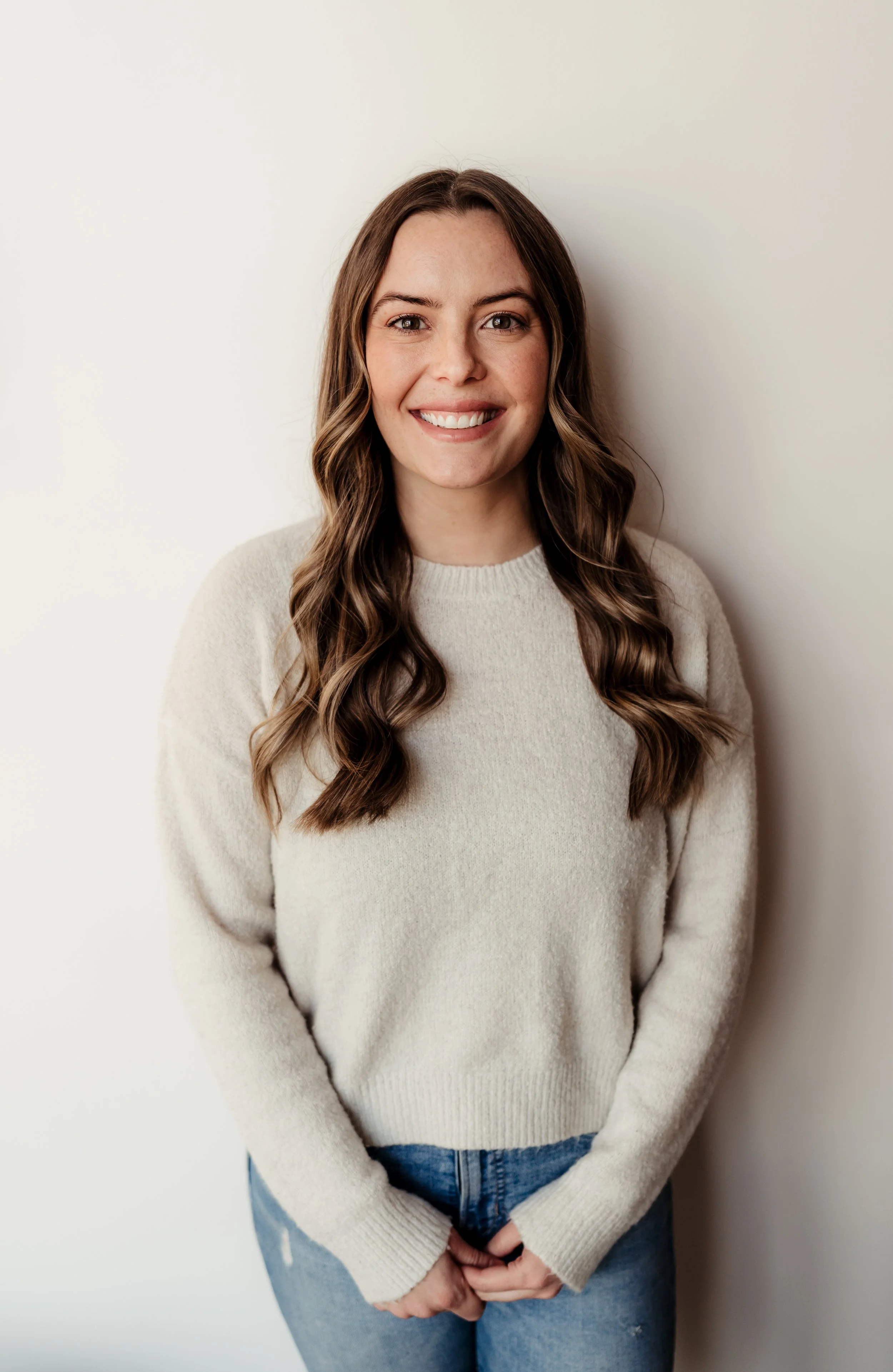 portrait of smiling woman in jeans and a sweater front of white wall