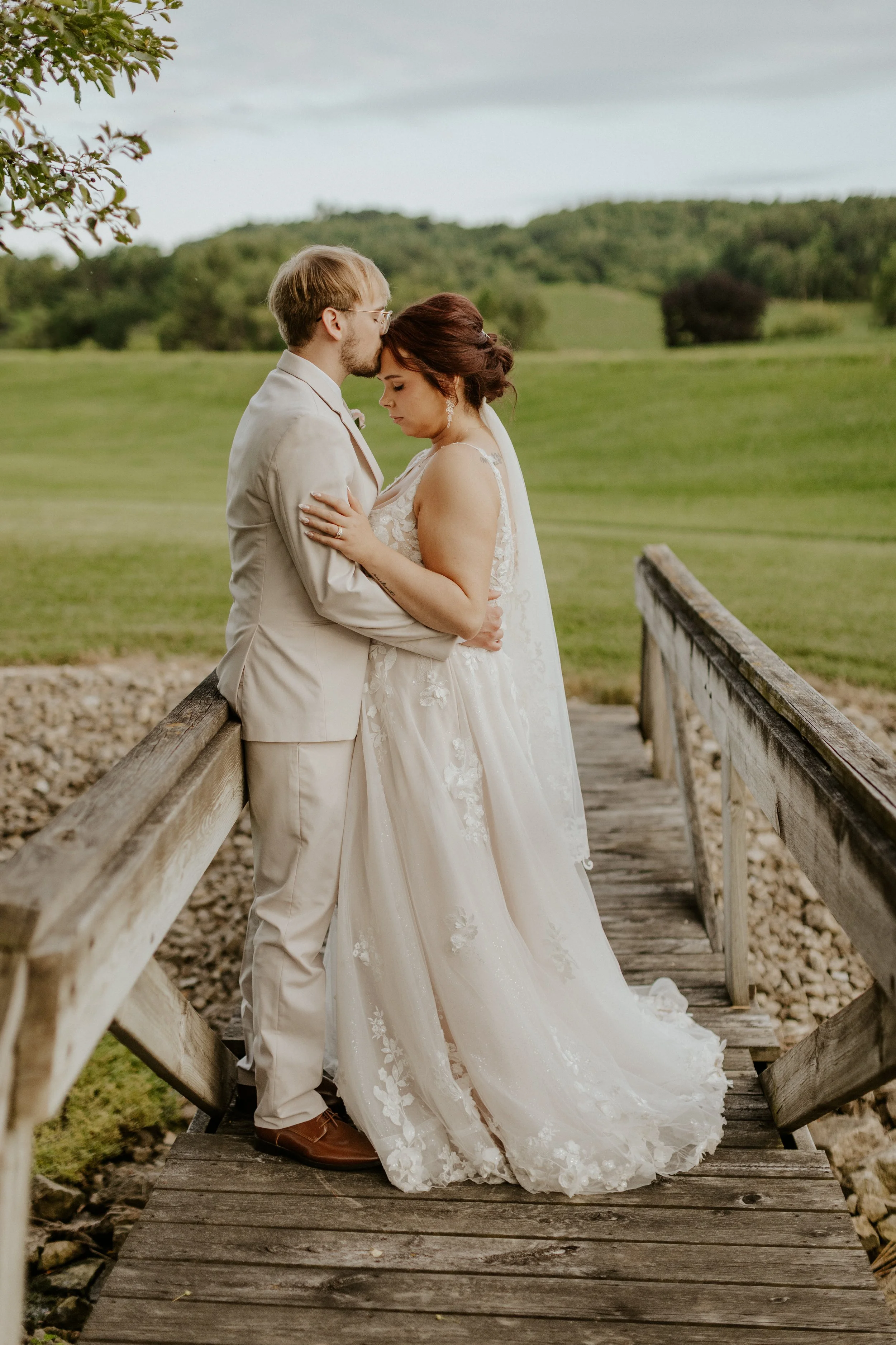 young couple in bridal attire kissing on bridge