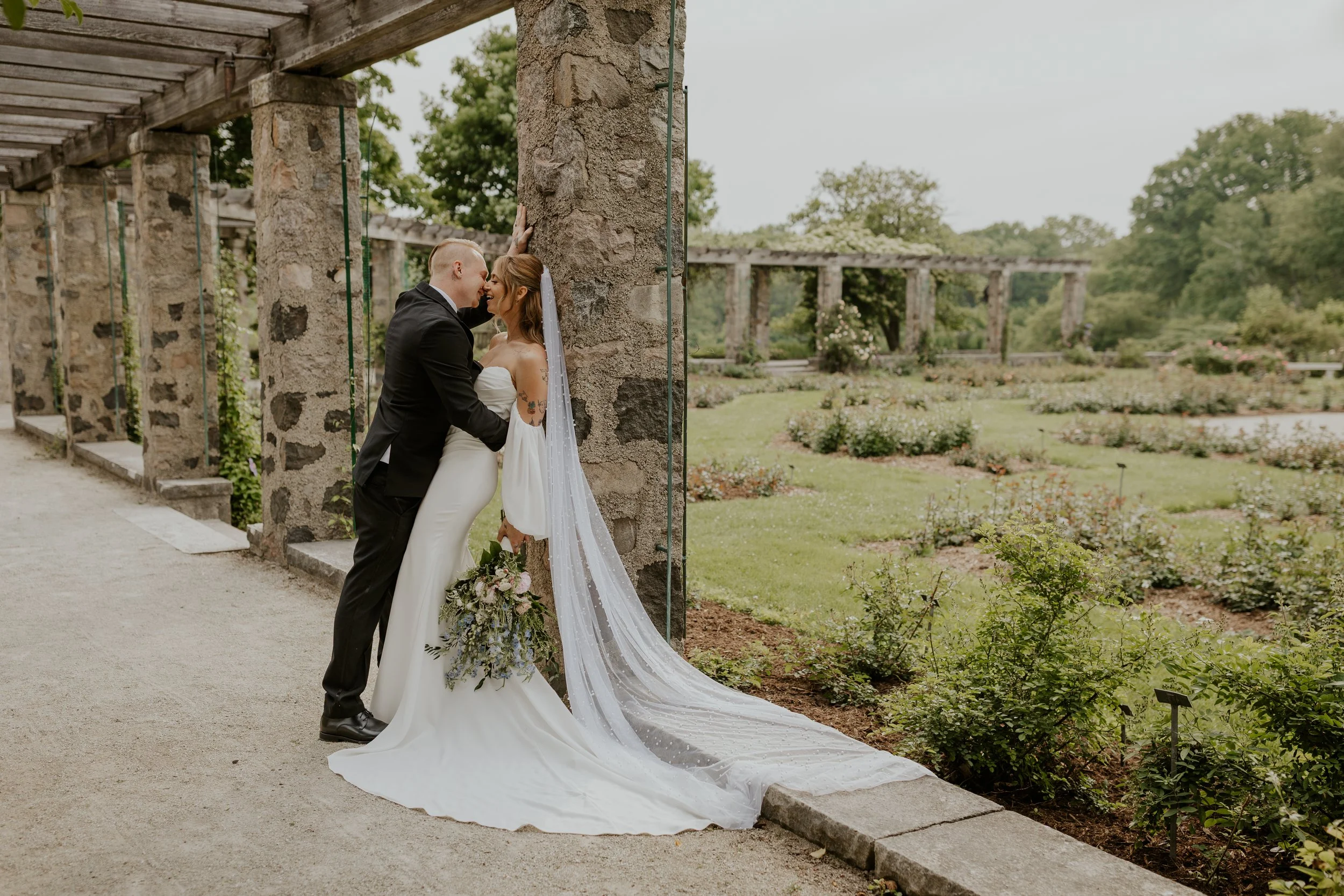couple kissing and leaning against stone wall of pergola