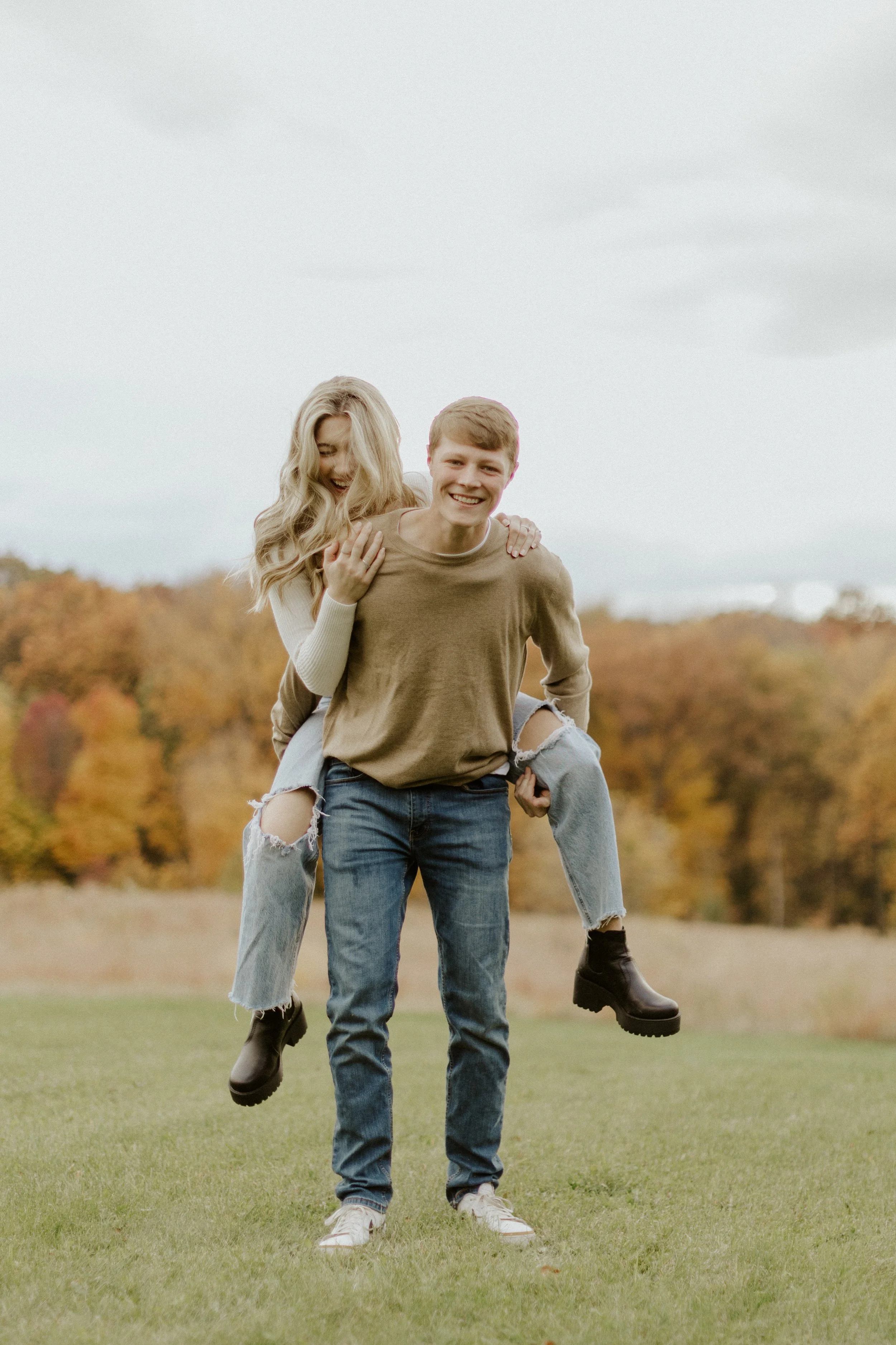 young couple laughing and playing piggy back in field during fall