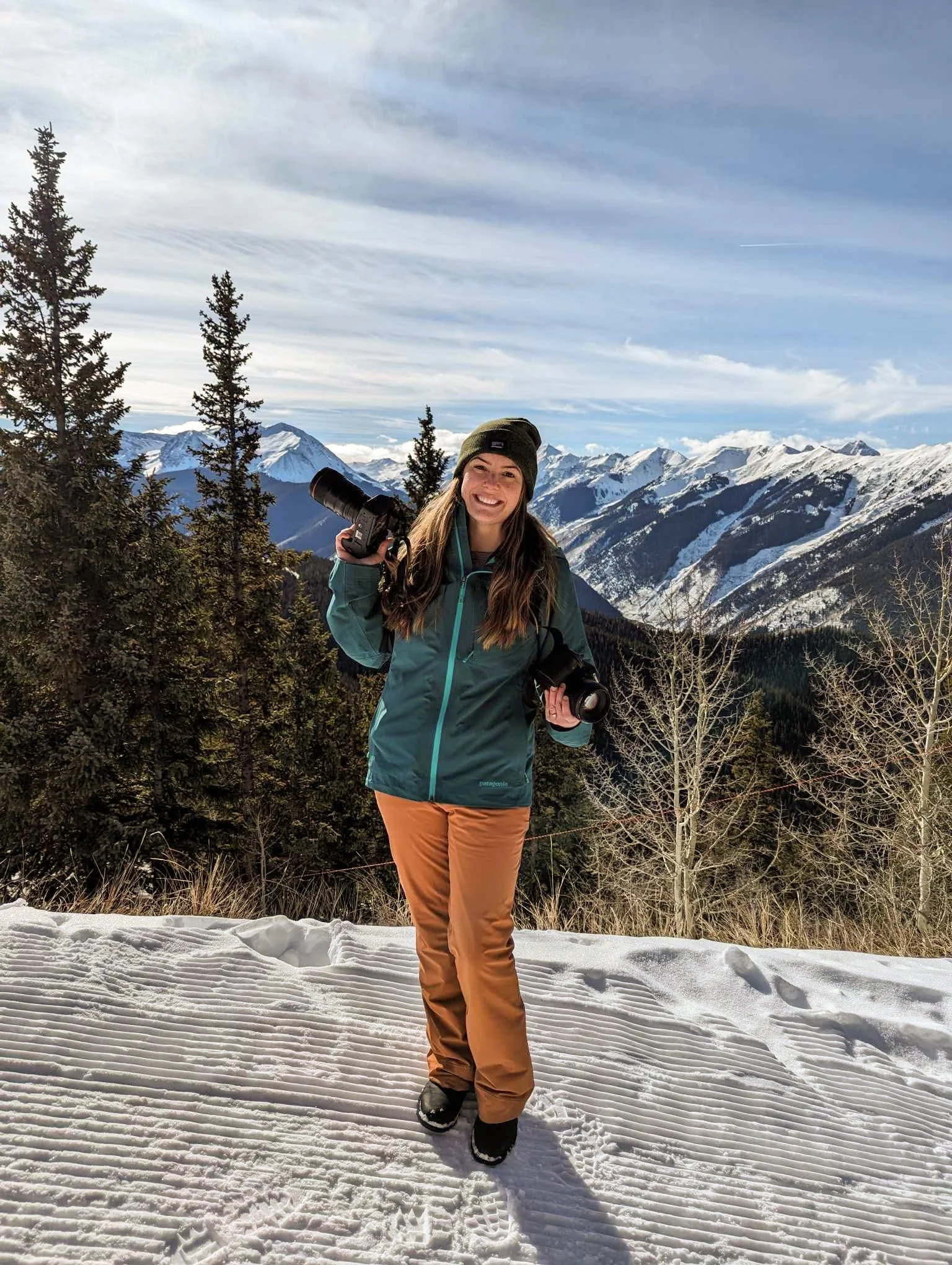 Woman dressed in ski gear holding two dslr camera on top of a snowy mountain in Aspen, CO