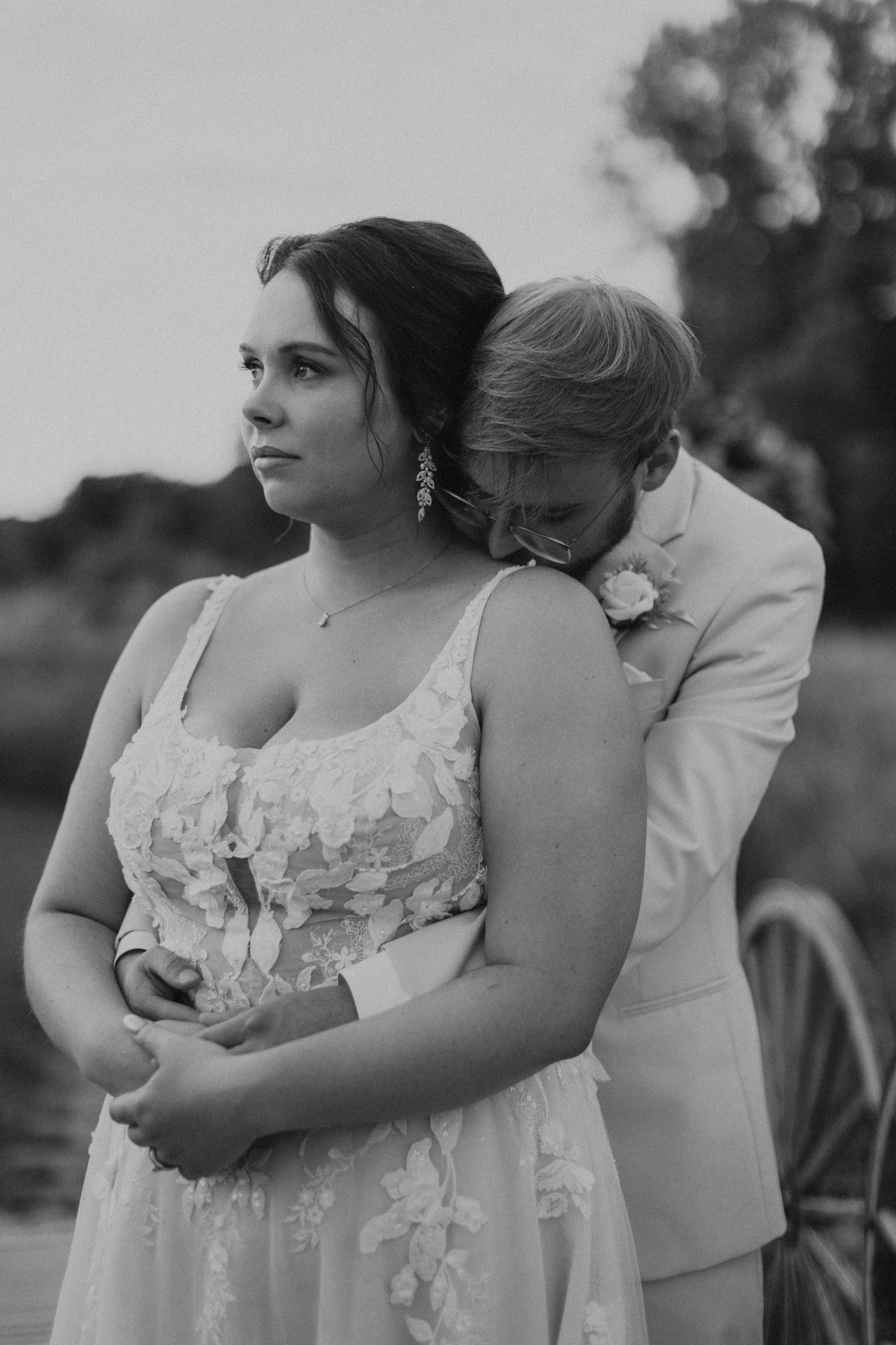 groom embracing bride from behind and kissing the top of her shoulder