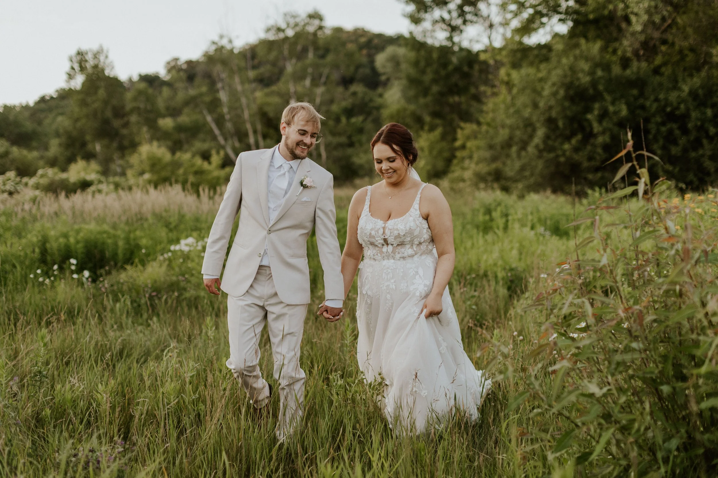 eloping couple laughing and holding hands while walking through the grass