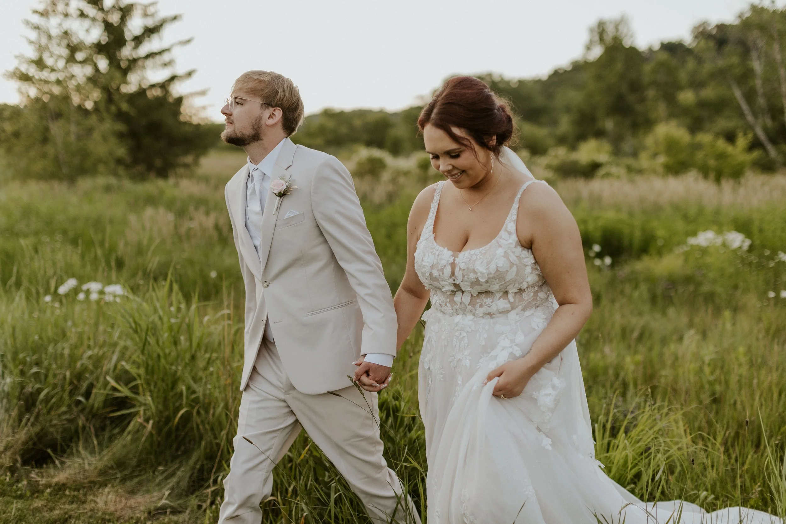 bridal couple holding hands and walking through meadow