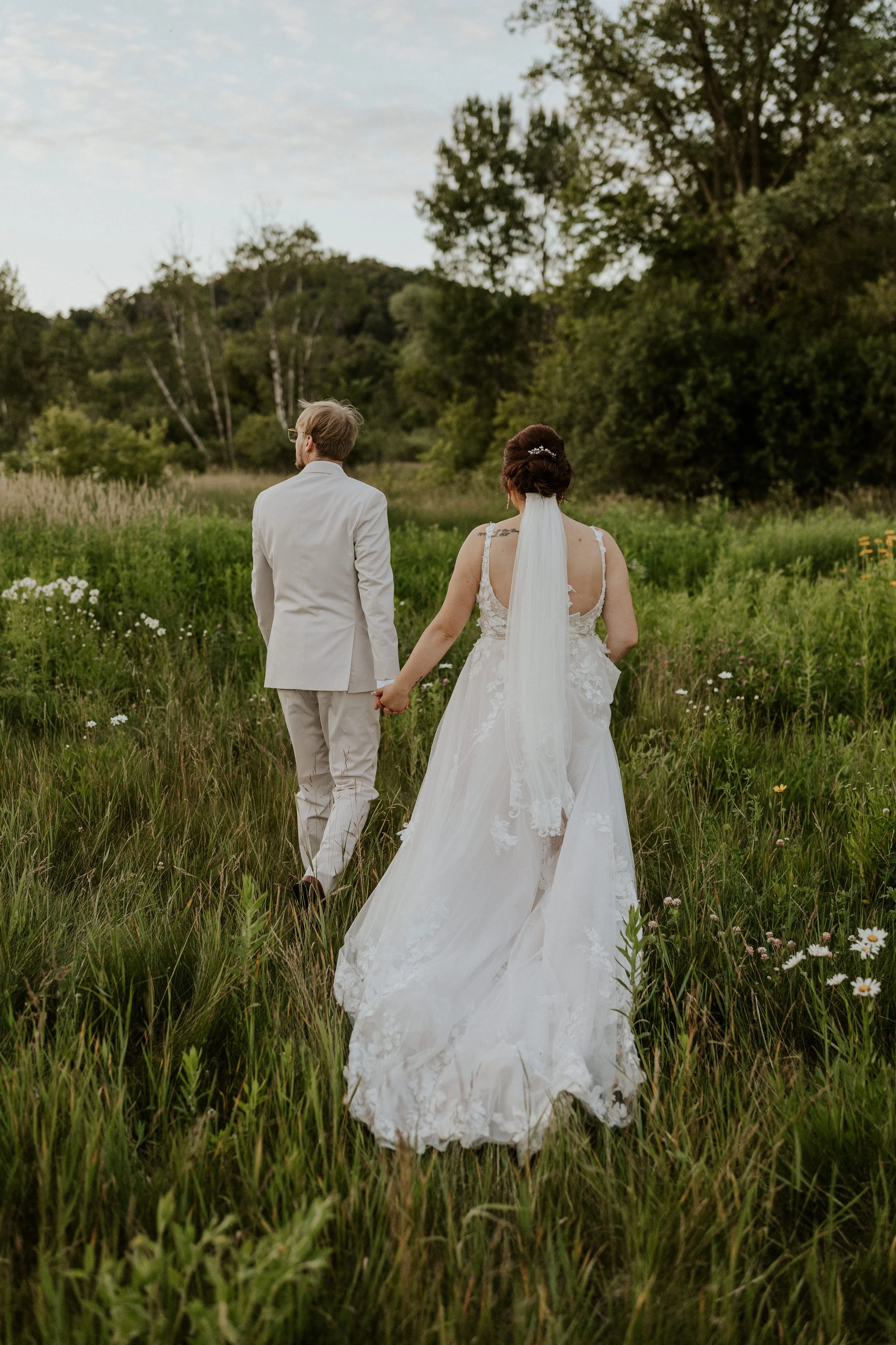 bridal couple walking away from camera in a grassy meadow