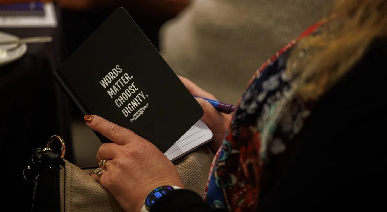 Person writing in a notebook with "Words Matter. Choose Dignity." on the cover