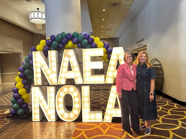 Tami in front of a lighted sign that reads "NAEA NOLA"