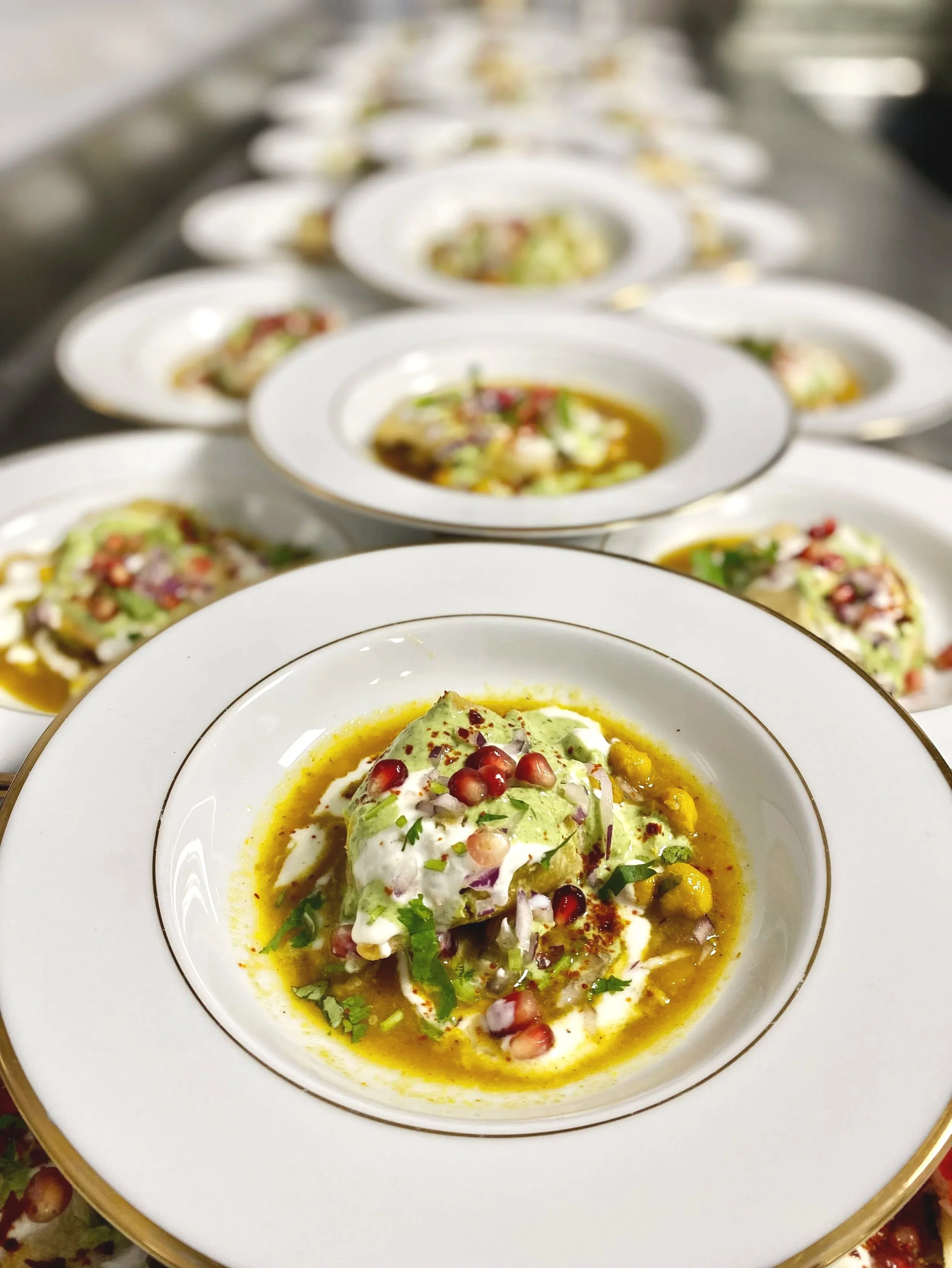 Assiettes de soupe avec des garnitures de légumes, herbes, et graines de grenade, alignées sur une surface.