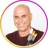 Smiling bald man with four paintbrushes tucked into his shirt pocket, wearing a dark top, against a plain white background with a colored circular border.