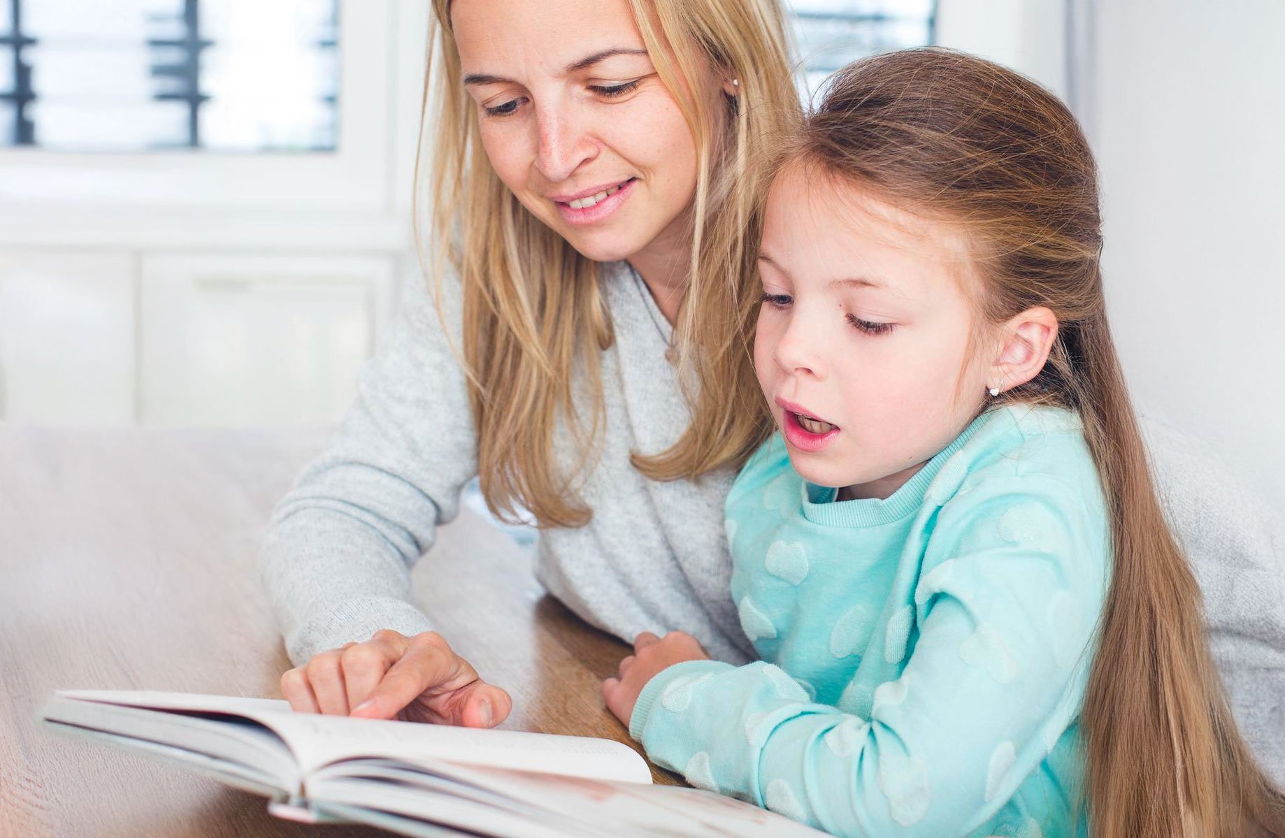 Mother and daughter practicing phonics together while reading a book