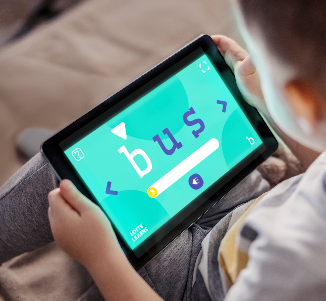 A child holding a tablet showing the word bus on the Lotty Learns Phonics Factory blending tool practicing sounding out words