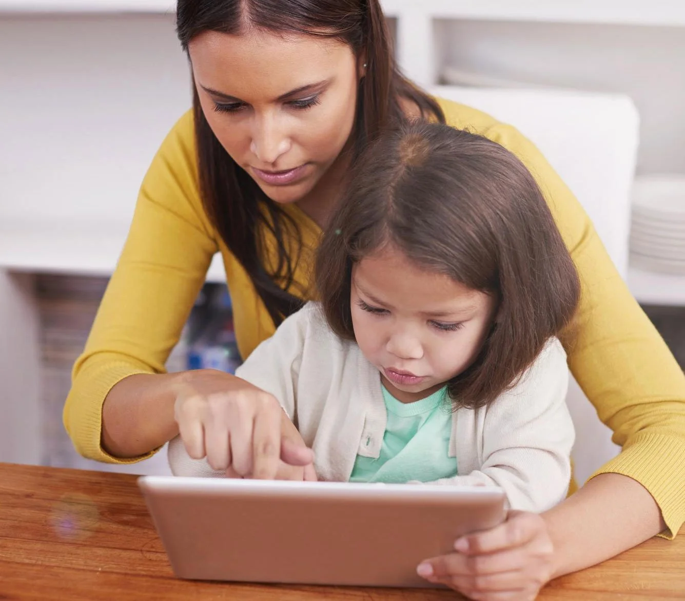 A mother and young child sitting together at a table with the parent actively pointing and guiding the learning session