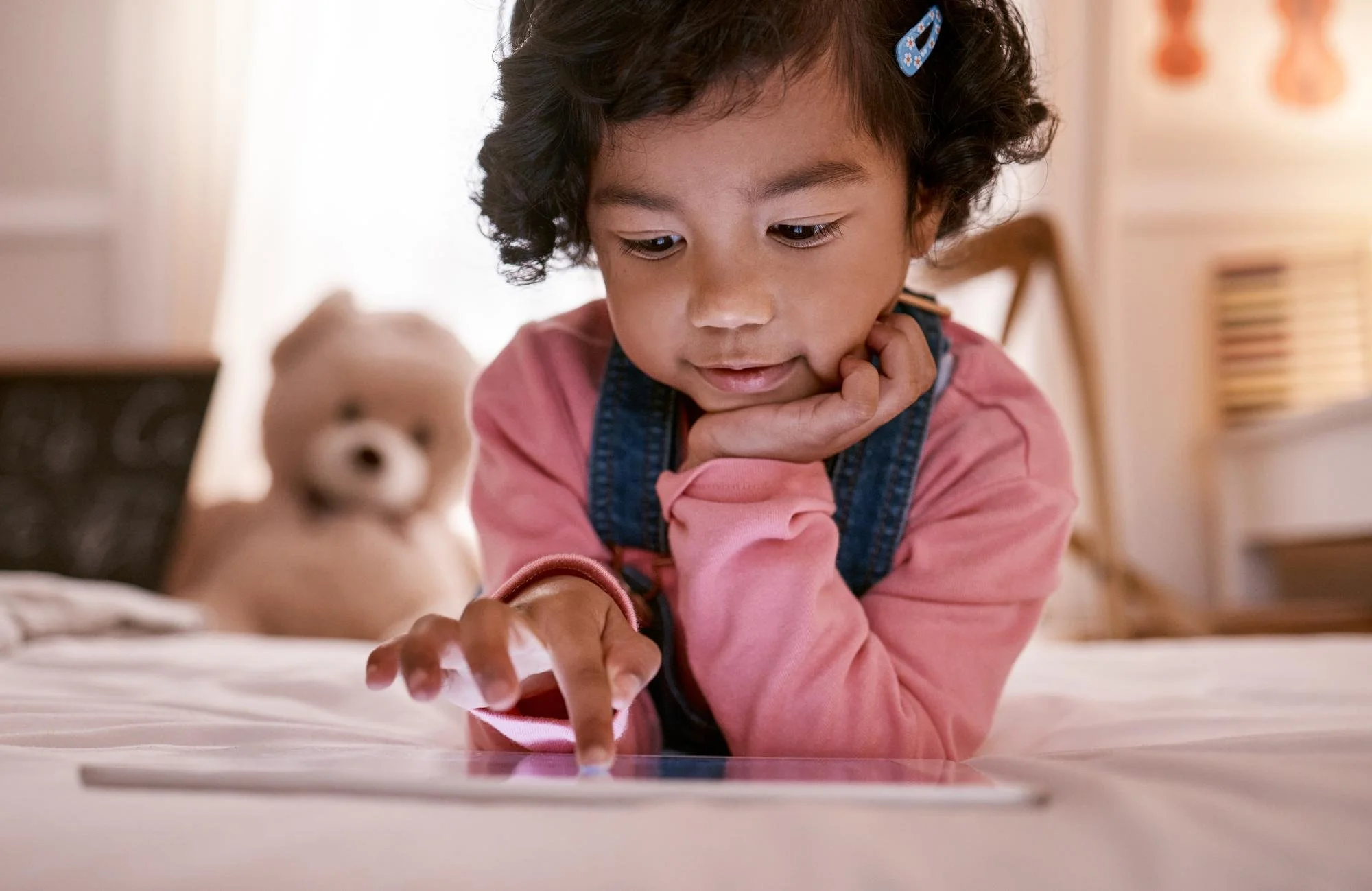 A young child lying alone absorbed in a tablet using a learning app without a parent present