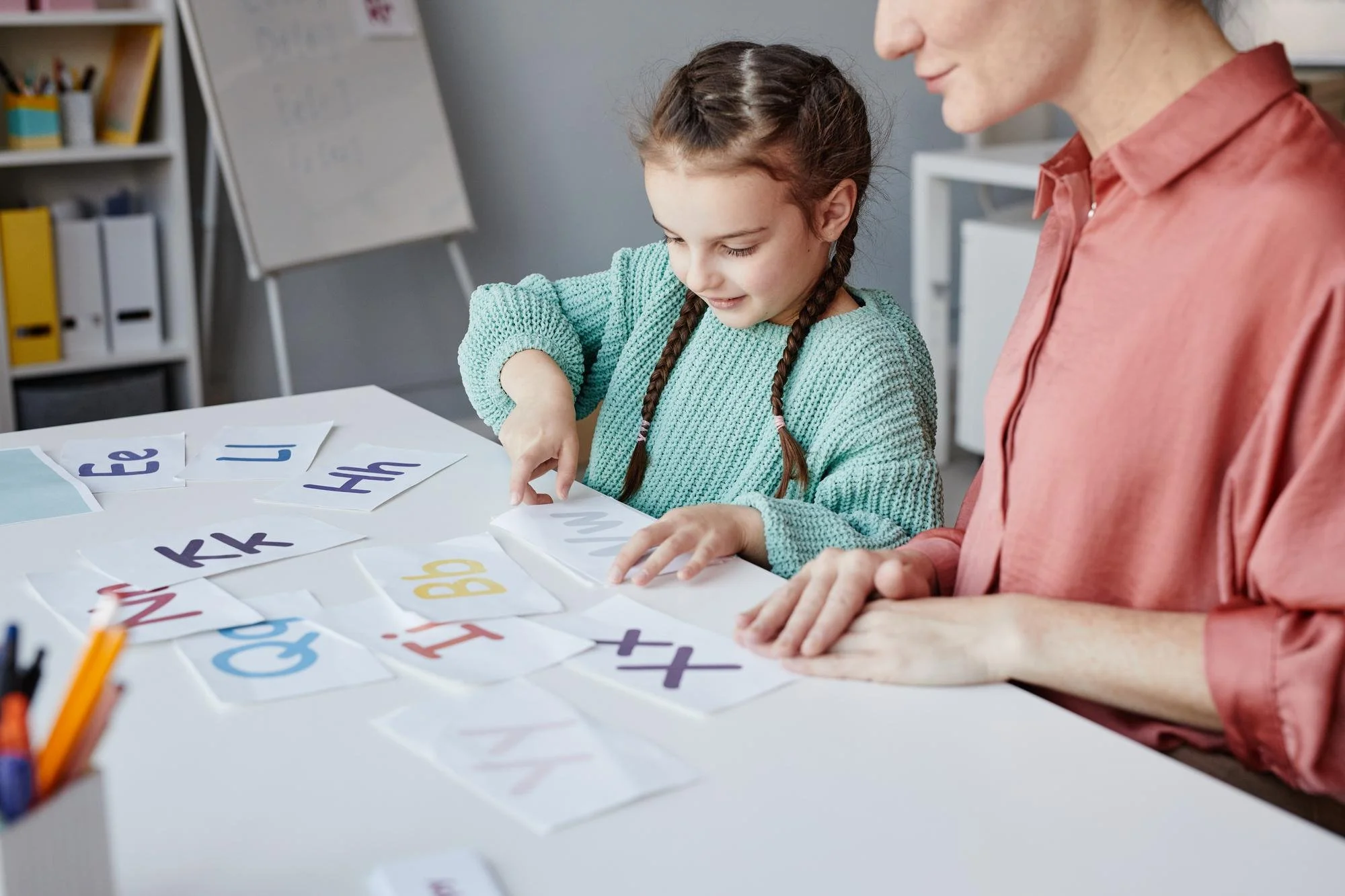 A girl pointing at letter flashcards while an adult watches during early phonics and letter sound practice