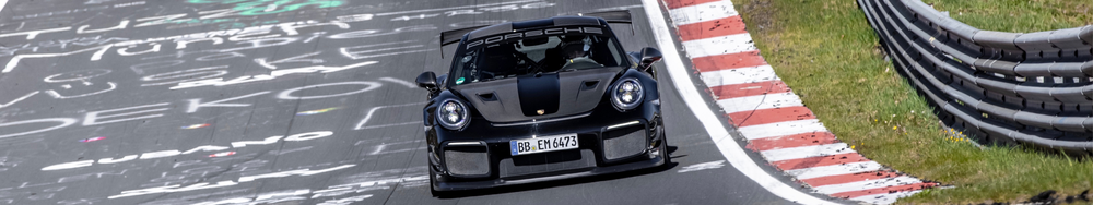 A black Porsche 911 racing car on a race track, passing through a curve with red and white striped curb and a protective barrier on the side.