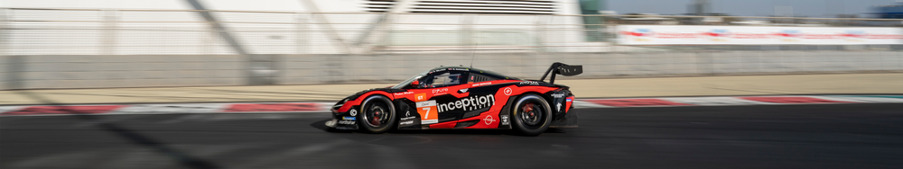 A race car on a racetrack with blurred background and black fence, moving at high speed.