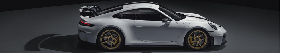 A white Porsche 911 GT3 sports car with black accents and gold wheels, viewed from the side on a dark background.