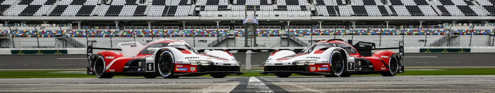 Two race cars on a track with empty grandstands in the background, positioned side by side facing the camera.