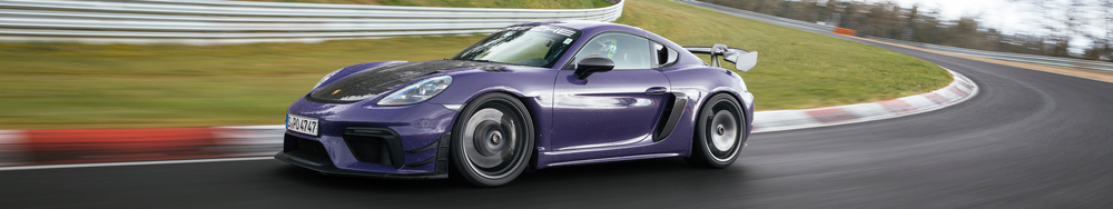 A purple Porsche 718 Cayman GT4 race car driving on a race track with blurred background.
