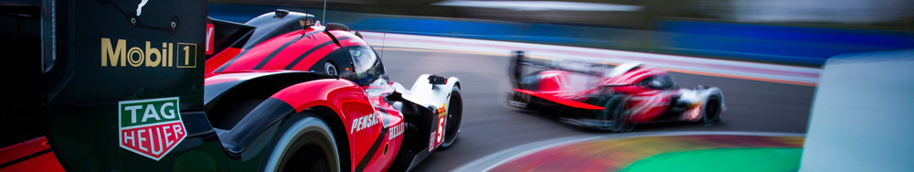 Two race cars speeding on a track, one close to the camera and another further down the track, both with red and black designs.