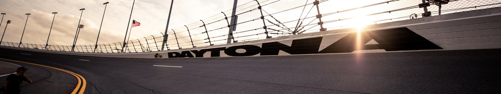 Daytona International Speedway with a person on the track and American flags, sunlight shining through the fence.