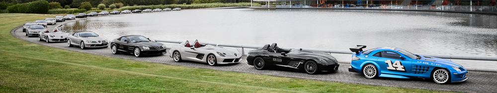 Lineup of sports cars parked along a lake, including various Mercedes-Benz models and a blue race car with the number 14.