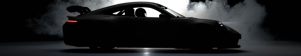 A black sports car with a rear spoiler, set against a dark, smoky background with a spotlight highlighting its silhouette.