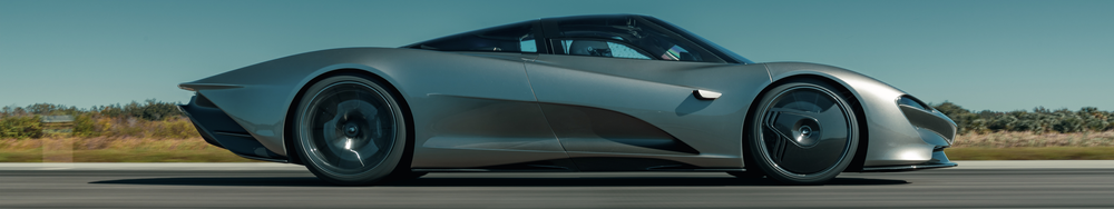 A sleek, futuristic silver sports car driving on a road with a blurred landscape background.