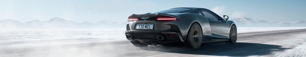 A black McLaren sports car driving on a snow-covered road with mountains in the background.