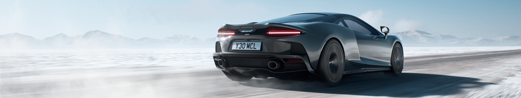 A black McLaren sports car driving on a snow-covered road with mountains in the background.