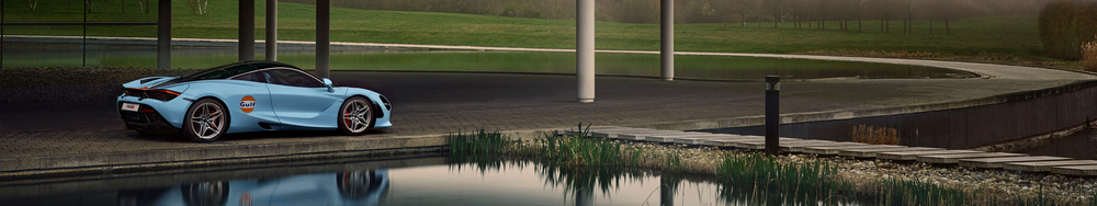 A light blue sports car with Gulf logo parked by a reflecting pond on a paved area with a grassy park in the background.