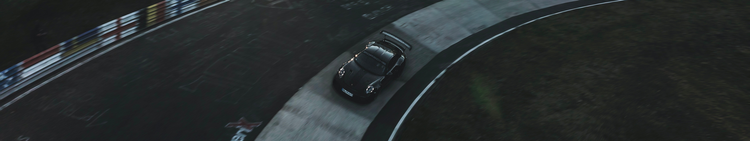 A black sports car, likely a Porsche, on a race track, viewed from above in a bird's eye perspective, with curbing painted in white, red, and blue on the left side.