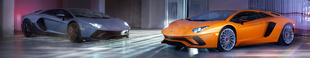 Two Lamborghini sports cars, one gray and one orange, parked indoors under colorful lighting.