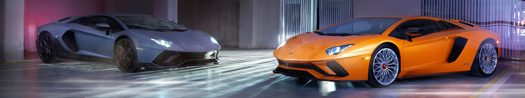 Two Lamborghini sports cars, one gray and one orange, parked indoors under colorful lighting.